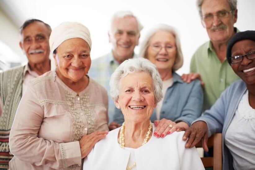 a smiling elderly woman supported by a group of people